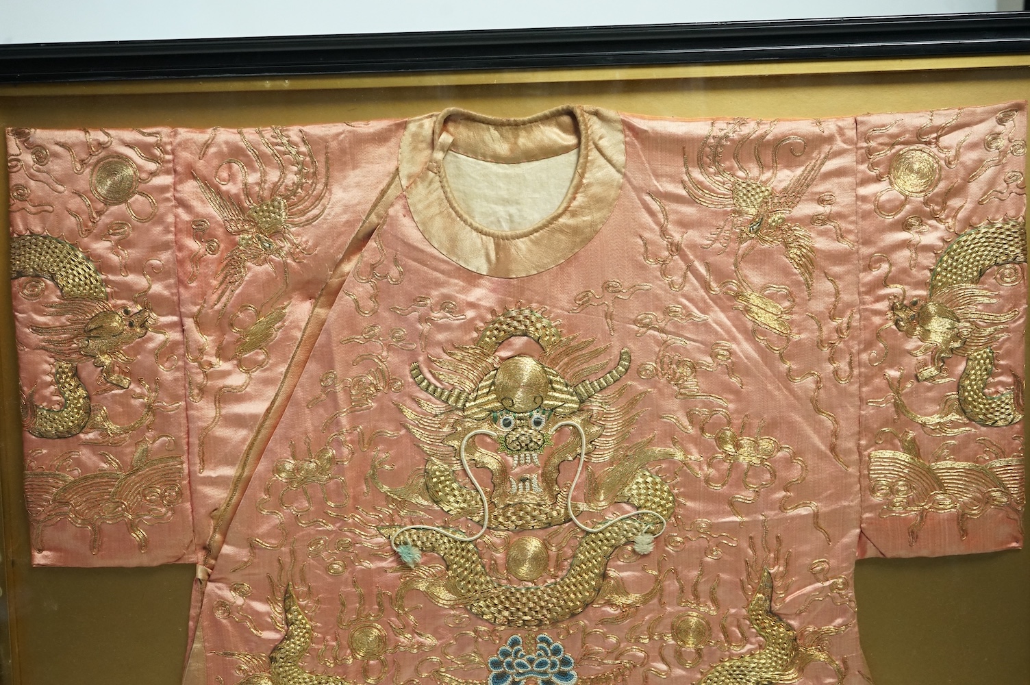 A framed late 19th early 20th century Chinese pink silk and gold embroidered dragon jacket. The dragons embroidered with raised couched gold thread work, surrounded by Phoenix and auspicious symbols. Jacket 69cm wide x 7